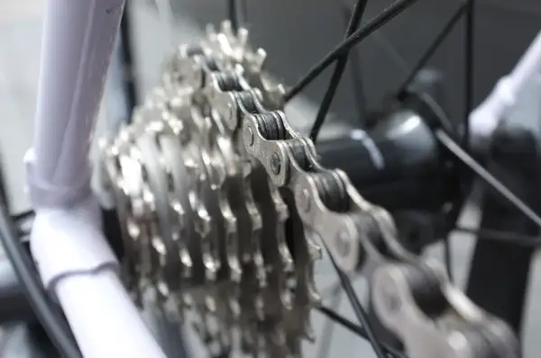 Biała rama roweru, metalowy łańcuch i zębatki tworzą mechanizm wolnobiegu.