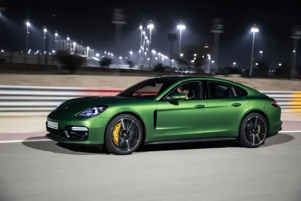 Zielony Porsche Panamera GTS pędzi nocą po torze wyścigowym, oświetlonym jaskrawymi światłami.