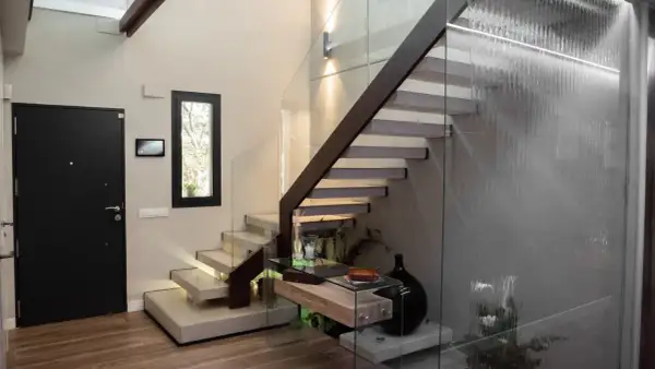 Modernas escaleras interiores prefabricadas con peldaños flotantes de hormigón y barandilla de cristal. Una cascada interior ilumina el espacio.
