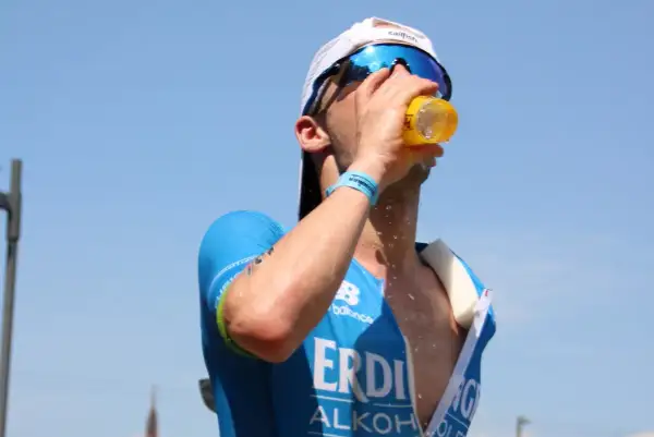 Triathlet trinkt bei heißem Wetter. Sport bei Hitze erfordert Flüssigkeitszufuhr.