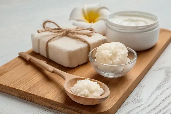 Jabón artesanal, crema y exfoliante de **grasa de karité** en cuchara de madera, sobre tabla de bambú.