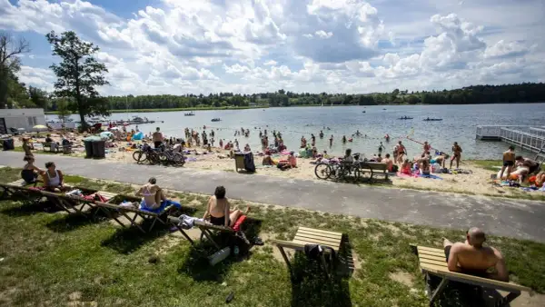 Tłum ludzi odpoczywa nad jeziorem w Poznaniu, opalając się na plaży i kąpiąc w wodzie.