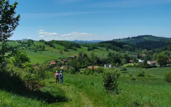 Dwie dziewczynki wędrujące po zielonych wzgórzach Gór Sowich z widokiem na wieś.