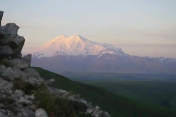 Majestatyczne gory z elbrusem w różowym świetle zachodzącego słońca. Na pierwszym planie skaliste zbocze.