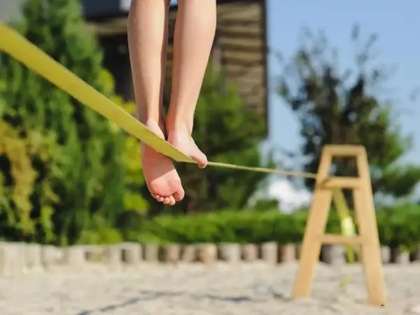 Füße balancieren auf einer gelben Slackline, die an einem Holzgestell befestigt ist.