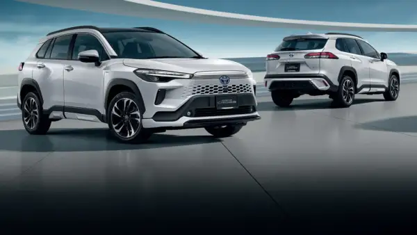 Dwa białe SUV-y Toyota Corolla Cross 2025 stoją na betonowej podłodze, jeden z przodu, drugi z tyłu.