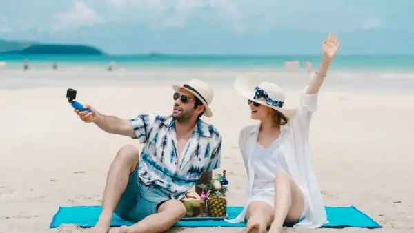 Para na plaży robi selfie z kamerką GoPro, ciesząc się wakacjami. W tle błękitne morze i niebo.