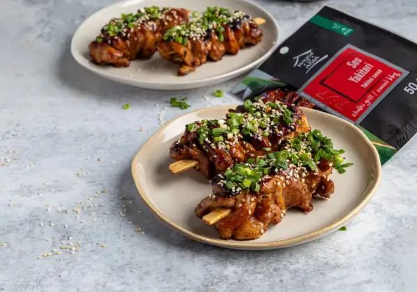 Pyszne yakitori na patyczkach, polane sosem i posypane sezamem i szczypiorkiem. Obok opakowanie sosu Yakitori.