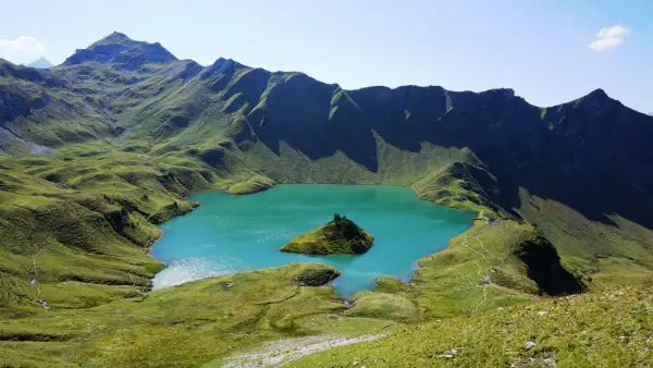 Türkiser Bergsee in Deutschland mit einer kleinen Insel, umgeben von grünen, schattigen Berghängen.