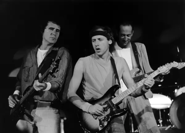 Trzech członków Dire Straits gra na gitarach podczas koncertu.