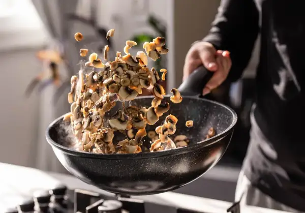 Man salteando champiñones en una sartén, mostrando cómo cocinar las setas para un plato delicioso.