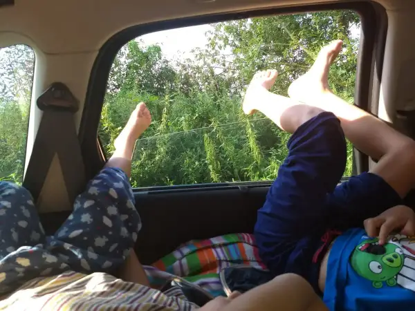 Dzieci odpoczywają, wyciągając nogi przez okno samochodu. Wygodne spanie w samochodzie podczas podróży.