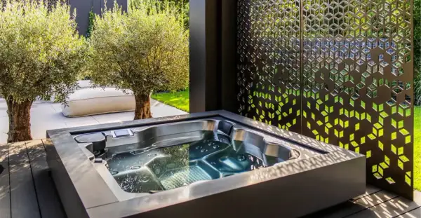 Un jacuzzi moderno en un jardín con olivos y un biombo decorativo. El lugar perfecto para un momento de relax y qué es un chill out.
