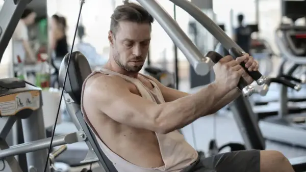 Mann trainiert im Fitnessstudio, um schnell zuzunehmen. Er sitzt auf einem Gerät und drückt die Griffe nach vorne.