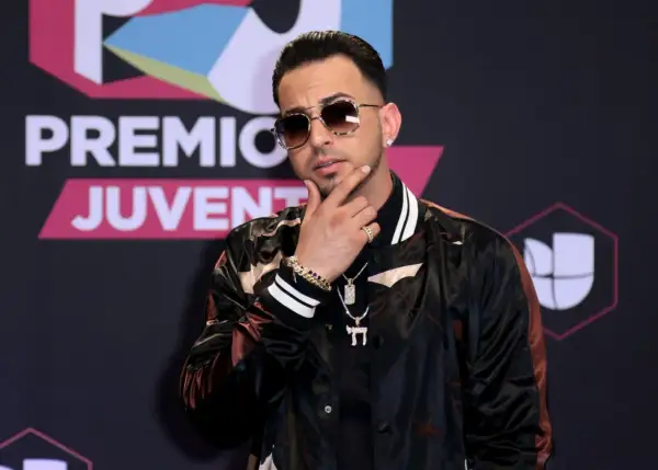 Justin Quiles poses with his hand on his chin, wearing sunglasses and a stylish jacket at Premios Juventud.