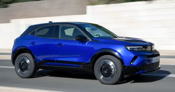 Błękitny Opel Mokka 2024 z czarnym dachem pędzi po drodze, prezentując swój nowoczesny design i dynamiczną sylwetkę.