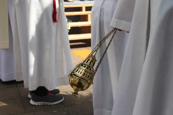Osoba w białej szacie trzyma złote kadzidło na łańcuszku.