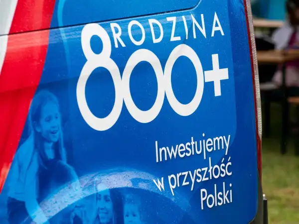 Niebieski baner z napisem "RODZINA 800+" i hasłem "Inwestujemy w przyszłość Polski". Widoczne uśmiechnięte dzieci.