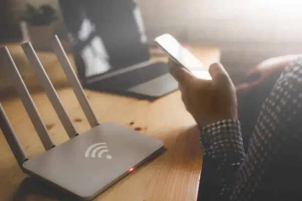 Router i smartfon na biurku. Zastanawiasz się, jak sprawdzić na jakie strony ktoś wchodził wifi?