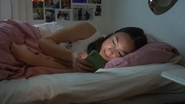 Ung flicka i sängen med mobilen, ett exempel på nackdelar med sociala medier som påverkar sömnen.