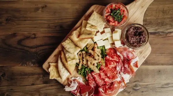 Un beau plateau de charcuterie avec jambon, salami, fromages, pain, olives et tomates.