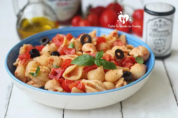 Un piatto di pasta con ricotta e pomodorini freschi, arricchito da olive nere e basilico.