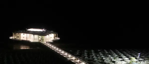 La Rotonda a Mare di Senigallia illuminata di notte, con la passerella che conduce all'edificio e la spiaggia con ombrelloni chiusi.