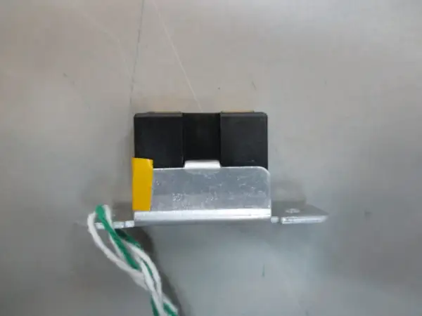Mały, czarny element z żółtym akcentem i przewodami, przypominający wtyczkę RGB, zamontowany na metalowej płytce.