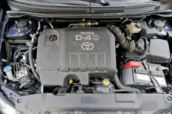 Silnik D-4D w Toyocie Corolla E12. Widoczny jest plastikowy kolektor dolotowy, akumulator i inne elementy komory silnika.