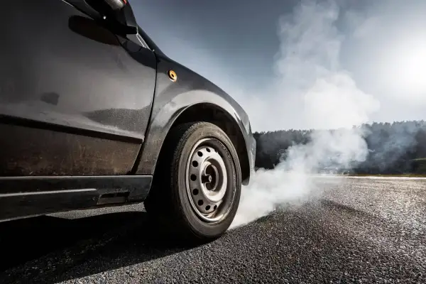 Une voiture freine brusquement, dégageant une épaisse fumée blanche. L'odeur de brûlé de plaquette de frein neuve emplit l'air.
