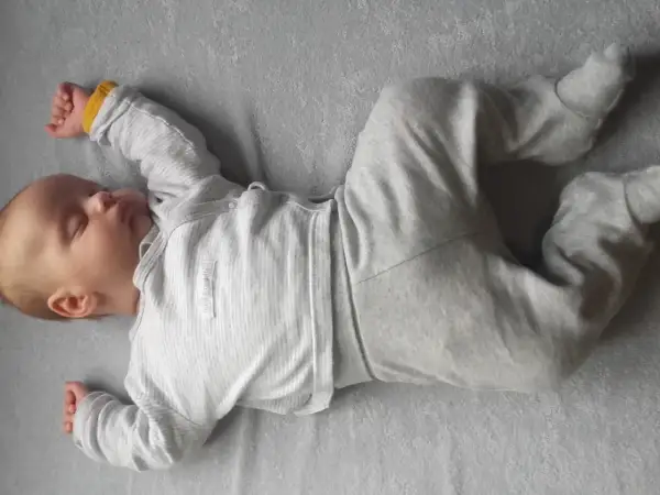 Śpiące niemowlę w szarym pajacyku leży na boku. Jego nóżki są wykrzywione, co może wskazywać na nieprawidłowy siad niemowlaka.