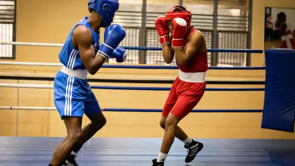 Two boxers in a ring, one in blue, the other in red, showcasing the disciplined footwork and defensive stance characteristic of the cuban boxing style.