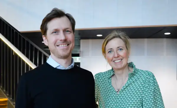 Tobias Sahlin ler glatt bredvid en kvinna i grön mönstrad blus. De står framför en trappa med belysning.