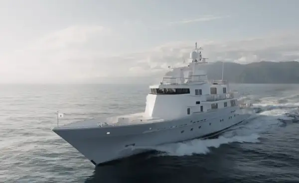 L'alessandro del bono yacht solca le onde con eleganza, un gioiello bianco su un mare calmo, con montagne sullo sfondo.