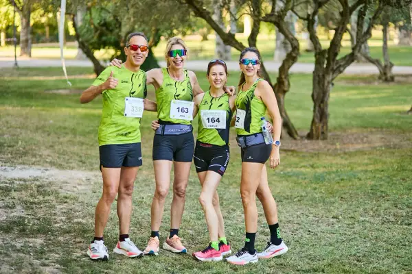 Cuatro corredores sonríen, listos para las carreras populares Zaragoza. Llevan camisetas verdes con dorsales y gafas de sol.