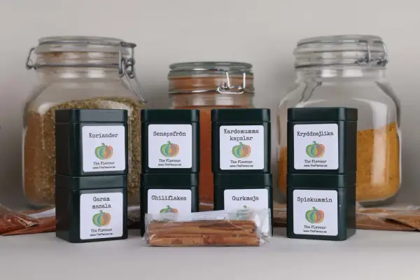 En samling mörkgröna burkar med kryddor, inklusive Garam Masala, som förbereder för en indisk kryddblandning.