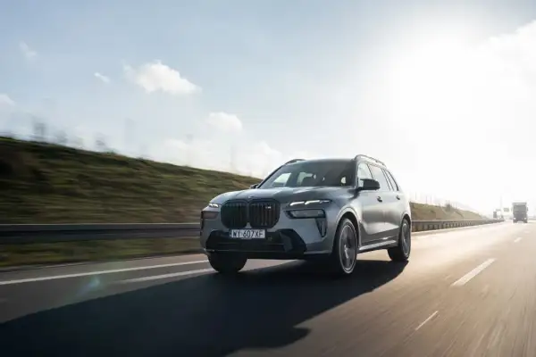 Szary BMW X7 M60i pędzi autostradą w słoneczny dzień.