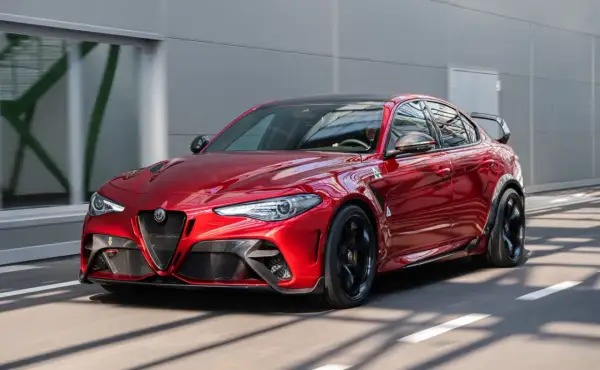 Czerwone Alfa Romeo Giulia GTAm z czarnym spojlerem i felgami pędzi po drodze.