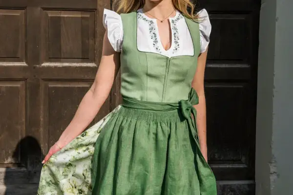 Tracht mit grünem Mieder und bestickter Bluse. Ein breiter Gürtel mit einer Schleife links betont die Taille.