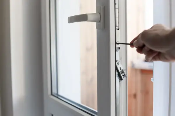 Main tenant utilise un tournevis pour régler une porte fenêtre 2 vantaux.
