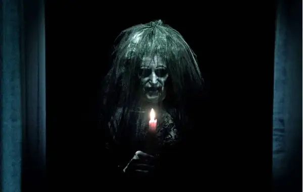 Przerażająca postać z zapaloną świecą, zapowiedź najstraszniejszych horrorów z jumpscare.
