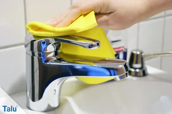 Hand poliert glänzenden Wasserhahn mit gelbem Tuch. Der Wasserhahn geht schwer, aber die Reinigung macht ihn wieder leichtgängig.