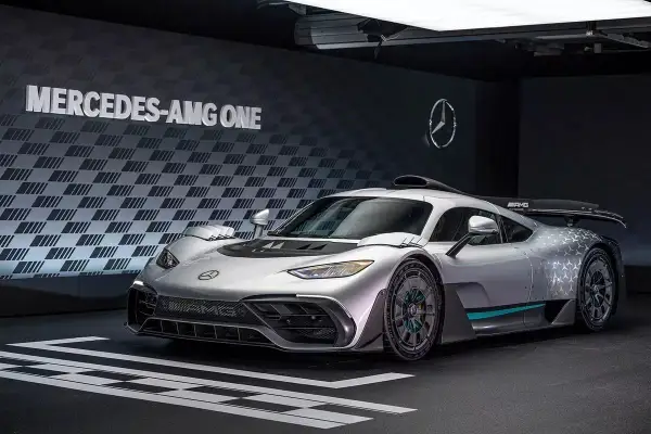 Srebrny Mercedes-AMG ONE, hiperauto z elementami wyścigowymi, prezentuje się na tle ściany z logo i napisem "MERCEDES-AMG ONE".