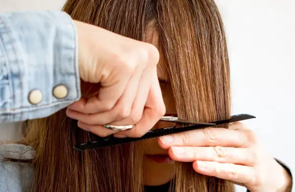 Eine Person schneidet sich mit Kamm und Schere die Haare, um Curtain Bangs zu kreieren.