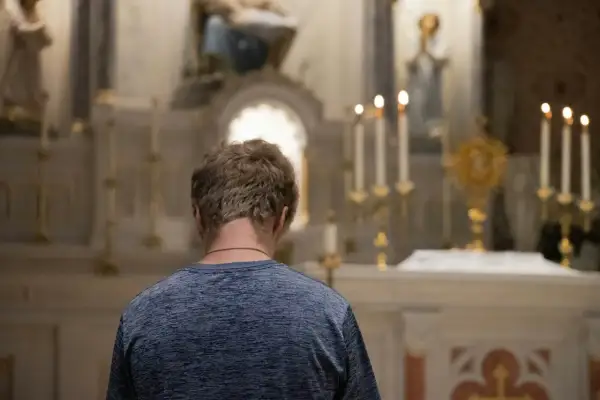 Młody mężczyzna klęczy przed ołtarzem, szukając rozgrzeszenia. Stosunek przerywany może być tematem jego modlitwy.