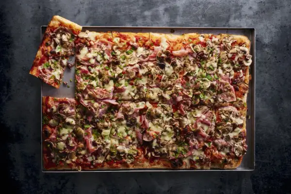 Pyszna pizza domowa przepis na blachę z szynką, pieczarkami i oliwkami, posypana serem i natką pietruszki.