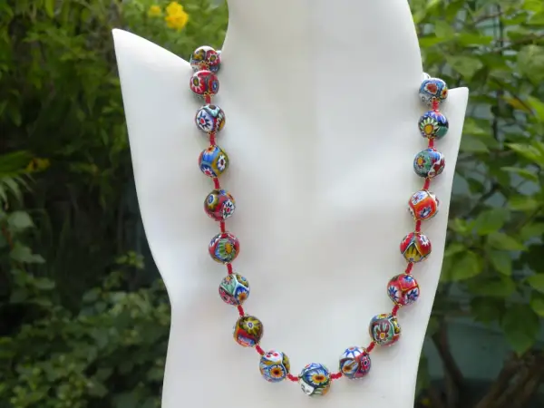 Colgantes de cristal de Murano, un collar vibrante con cuentas esféricas multicolores, cada una con un diseño floral único, sobre un fondo verde exuberante.