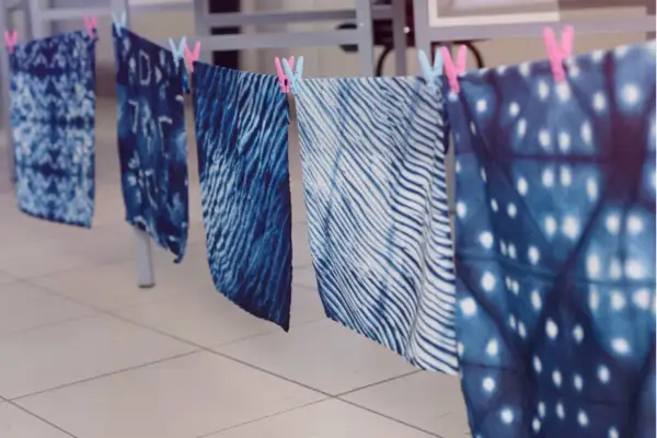 Stoffbahnen mit verschiedenen blauen Batik-Techniken trocknen an einer Leine. Muster wie Wellen, Punkte und abstrakte Formen sind sichtbar.