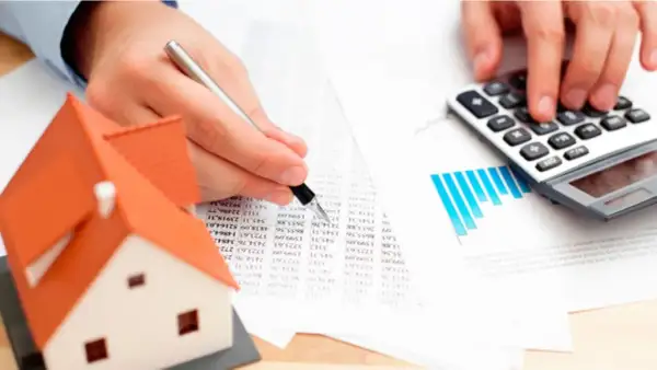 Man calculando el precio tasación vivienda con calculadora y modelo de casa.