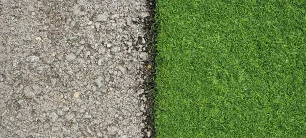 Superficie de asfalto gris y césped natural verde vibrante, mostrando la transición de poner césped artificial sobre césped natural.